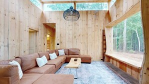 A wooden interior with a sectional sofa, a coffee table, and a large window. - Idyllic Lakeside House With Outdoor Sauna, Patio and Firepit (Hope)