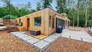A wooden cabin with a glass door, a small porch, and a concrete patio. - Idyllic Lakeside House With Outdoor Sauna, Patio and Firepit (Hope)