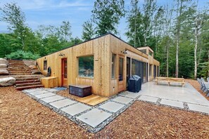 A wooden cabin with a glass door, a small porch, and a concrete patio. - Idyllic Lakeside House With Outdoor Sauna, Patio and Firepit (Hope)