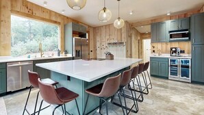 A modern kitchen with a large island, bar stools, and wooden paneling. - Idyllic Lakeside House With Outdoor Sauna, Patio and Firepit (Hope)