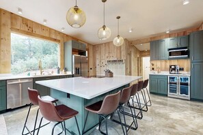 A modern kitchen with a large island, bar stools, and wooden paneling. - Idyllic Lakeside House With Outdoor Sauna, Patio and Firepit (Hope)