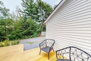 Une terrasse en bois avec deux chaises, un bâtiment blanc et un paysage boisé en arrière-plan.