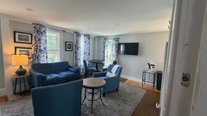 A living room with a blue sofa, a round table, and a TV mounted on the wall.