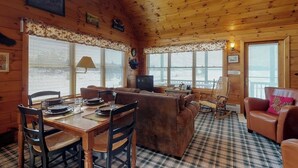 A cozy cabin interior with a dining area, a living room with a sofa and a television, and a rocking chair. - Moose Dance (Greenville)