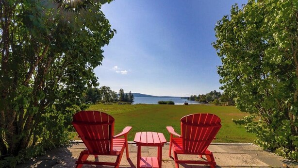 Two red Adirondack chairs and a small table on a patio with a view of a lake and distant mountains. - Moose Dance (Greenville)