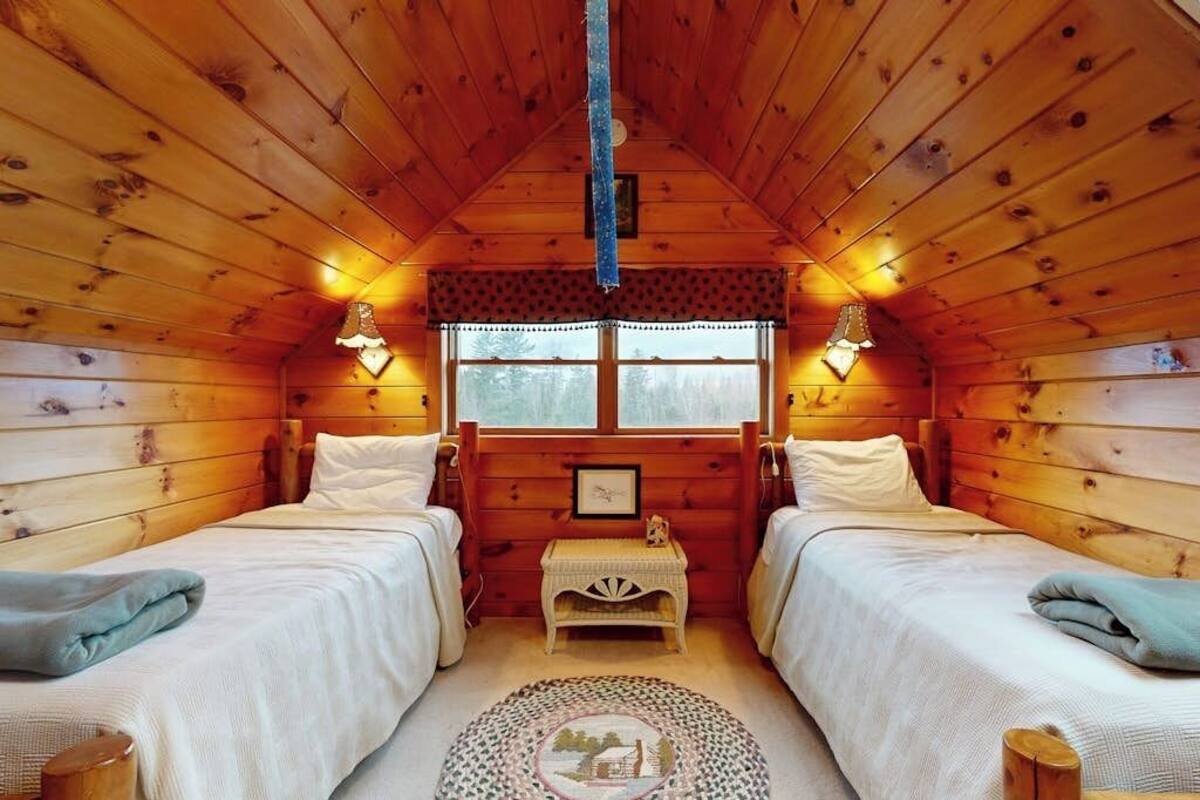 Una cabana amb dos llits, una taula petita i una finestra amb cortines.