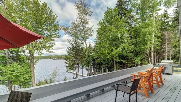 A deck with outdoor seating, overlooking a lake and surrounded by trees. - Lakefront Chalet-style Home With Large Deck, a Dock & Beautiful Lake Views (Greenville)
