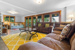 A spacious living room with a large sofa, a coffee table, and a fireplace. - Lakefront Chalet-style Home With Large Deck, a Dock & Beautiful Lake Views (Greenville)