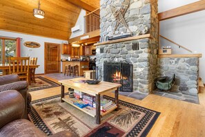 A cozy cabin interior with a stone fireplace, wooden furniture, and a dining area. - Lakefront Chalet-style Home With Large Deck, a Dock & Beautiful Lake Views (Greenville)