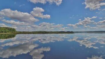 A calm lake reflecting clouds, surrounded by greenery and distant hills.