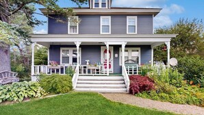 A two-story house with a porch, steps, and a garden. - Acadia Lights (Sullivan)