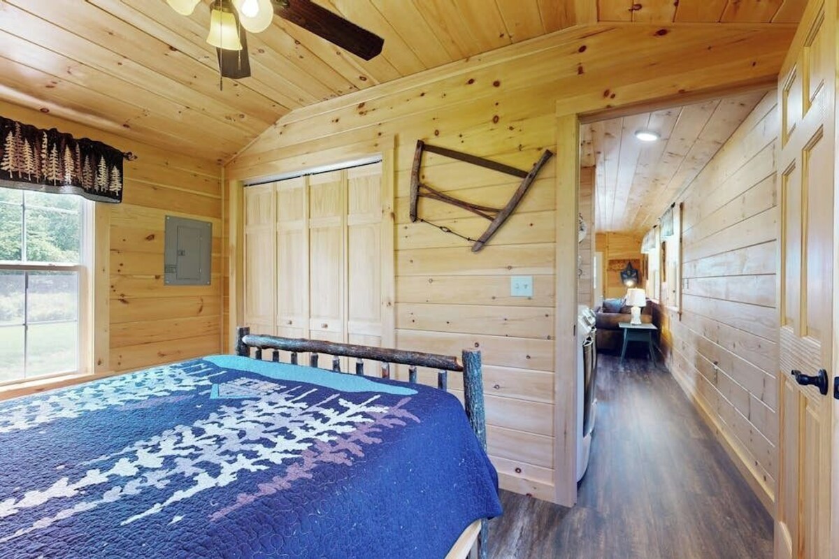 Ein Zimmer in einer Blockhütte mit einem Bett, einer Holzbalkendecke und einem Fenster.