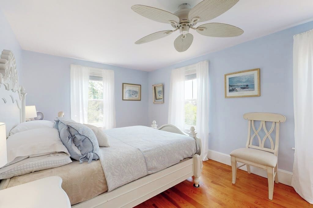 A bedroom with a bed, a chair, a ceiling fan, and framed pictures on the wall.