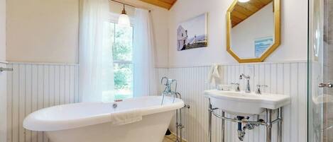 A bathroom with a freestanding bathtub, a sink with a mirror, and a window with curtains.