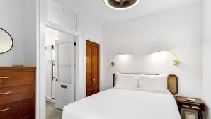 A bedroom with a bed, wooden dresser, two wall-mounted lamps, and a door leading to another room. - Kimball Apartment, Modern Studio on Main Street Ro (Rockland)