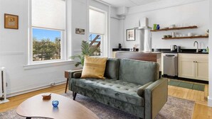 A living room with a sofa, a coffee table, and a view through large windows. - Kimball Apartment, Modern Studio on Main Street Ro (Rockland)