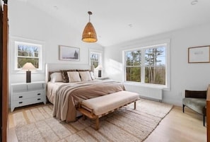 Ein Schlafzimmer mit einem großen Bett, einer Bank, einem Nachttisch, einer Lampe und einem Fenster.