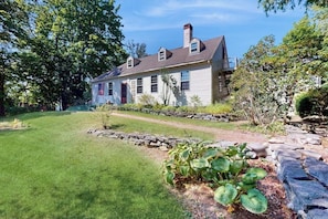 A two-story house with a stone pathway leading to the front door, surrounded by a well-maintained lawn and various shrubs. - Elegant Riverside Retreat With Breathtaking Views and Modern Comforts (Wiscasset)