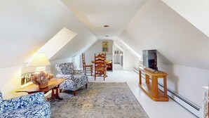 Un loft espacioso con techo alto, zona de comedor con mesa y sillas de madera, sofá, televisor sobre un mueble de madera y una alfombra estampada.