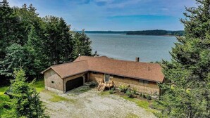 A single-story brick building with a garage, surrounded by trees and a lake view. - Renovated Oceanfront Home With Stunning View & Pebbly Beach - Snowbird-friendly (Tenants Harbor)