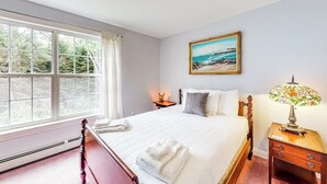 A bedroom with a large window, a bed with white linens, a nightstand with a lamp, and a painting on the wall. - Idyllic Waterfront Home With Furnished Deck, Grill, Sweeping Views & Private W/D (Waldoboro)