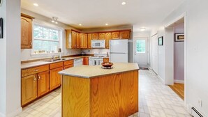 A kitchen with wooden cabinets, a central island, a microwave, and a refrigerator. - Idyllic Waterfront Home With Furnished Deck, Grill, Sweeping Views & Private W/D (Waldoboro)