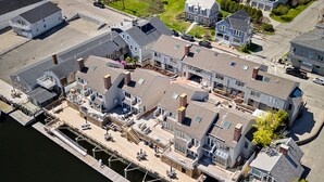An aerial view of a waterfront property with multiple buildings, dock, and a pedestrian bridge. - Bay View on Camden Harbor Condo 2br, 2 Baths, AC, Fireplace (Camden)