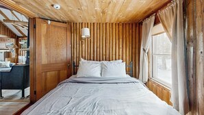 Ein Zimmer mit Holzwänden, einem Bett, einem Fenster mit Vorhängen und einer Wandlampe.