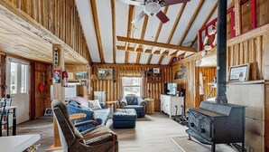 Ein rustikales Blockhaus-Interieur mit Holzwänden, einem Deckenventilator, einem Holzofen und einer gemütlichen Sitzecke.