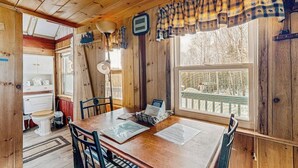 Ein Holzblockhaus-Interieur mit Esstisch, Stühlen, einem Fenster mit Aussicht und einer kleinen Küchenzeile.