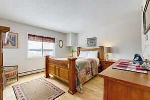 Ein Schlafzimmer mit einem hölzernen Bett, einem Nachttisch, einem Fenster mit Blick und einem Sessel.