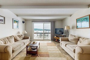 A living room with two sofas, a coffee table, a TV, and a balcony with a view. - Lakefront Condo on the Golf Course With Sweeping Views and Beach Access (Greenville Junction)