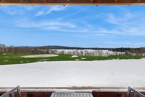 Ein verschneiter Außenbereich mit einer Holzterrasse und Blick auf eine ferne Landschaft.