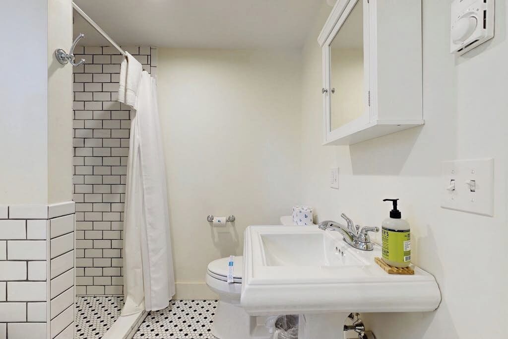 A bathroom with a white sink, a mirror, and a shower with a white curtain.