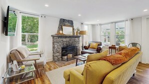 Ein Wohnzimmer mit Kamin aus Stein, einer Couch, einem Sessel und einem an der Wand befestigten Fernseher.