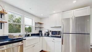 Eine moderne Küche mit weißen Schränken, einem Edelstahlkühlschrank, einer Mikrowelle und einer Kaffeemaschine.