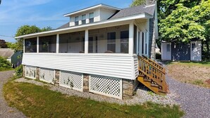 Ein eingeschossiges Haus mit einer überdachten Veranda, einem Steinsschornstein und einer Holztreppe, die zum Eingang führt.