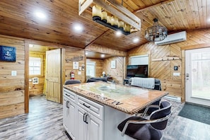 A wooden cabin interior with a kitchen island, dining area, and a large window. - Remodeled Cottage With AC, Private W/d, Full Kitchen, and High-speed Wifi (Boothbay Harbor)