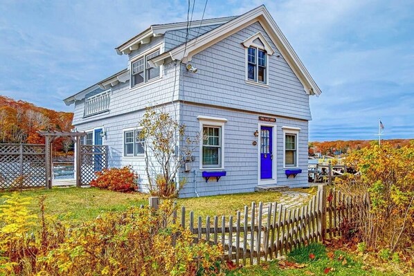 Une maison à deux étages avec une porte bleue, un petit porche et une clôture en bois.