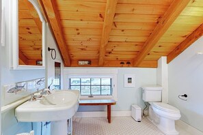 Une salle de bain avec un plafond en bois, un lavabo, des toilettes et une fenêtre.