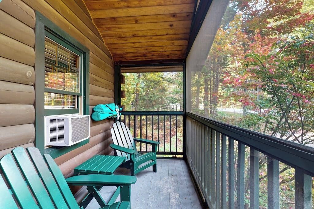 A wooden cabin with a porch, a table, two chairs, and an air conditioning unit.