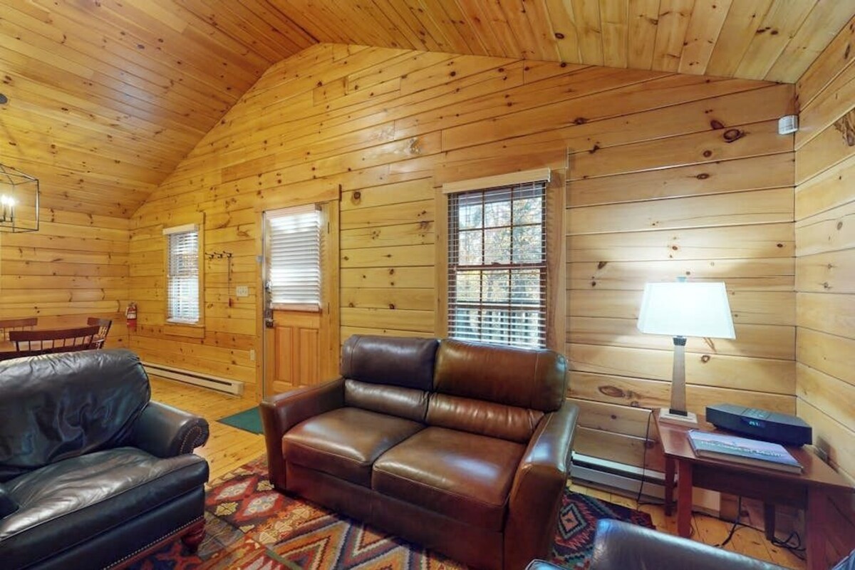 A log cabin interior with a leather sofa, a small table with a lamp, and a fireplace.