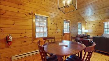 A wooden cabin interior with a dining table, chairs, a sofa, and a fireplace.