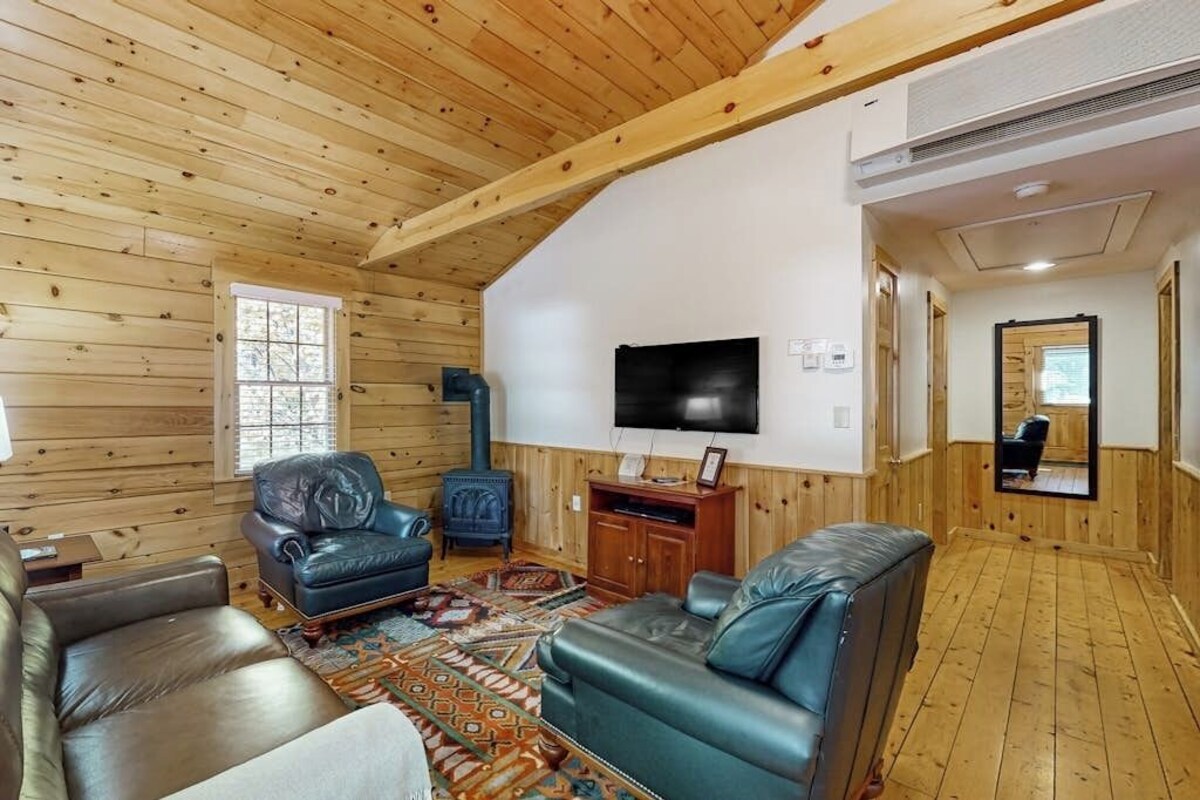 Interior de una cabaña de troncos con chimenea, sofás de cuero, televisor y un espejo.