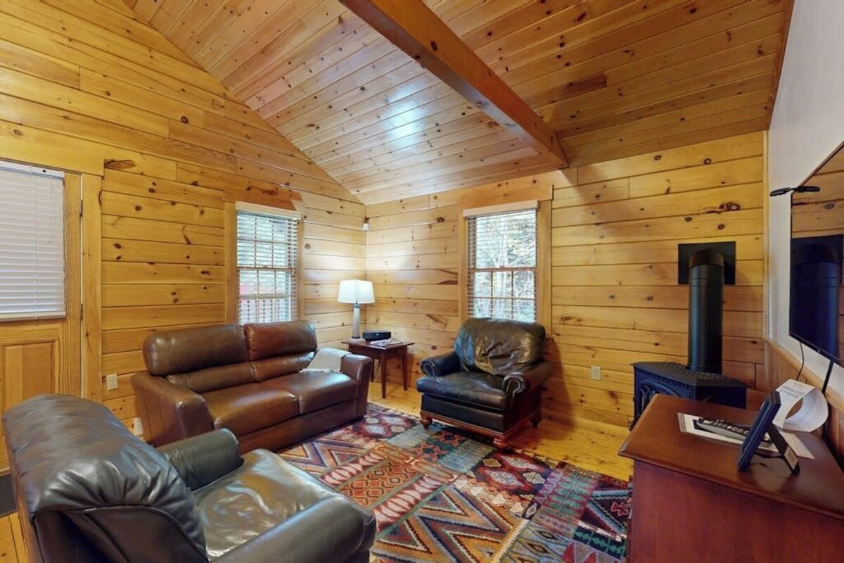 Interior de una cabaña de madera con sofá de cuero, sillón y chimenea.
