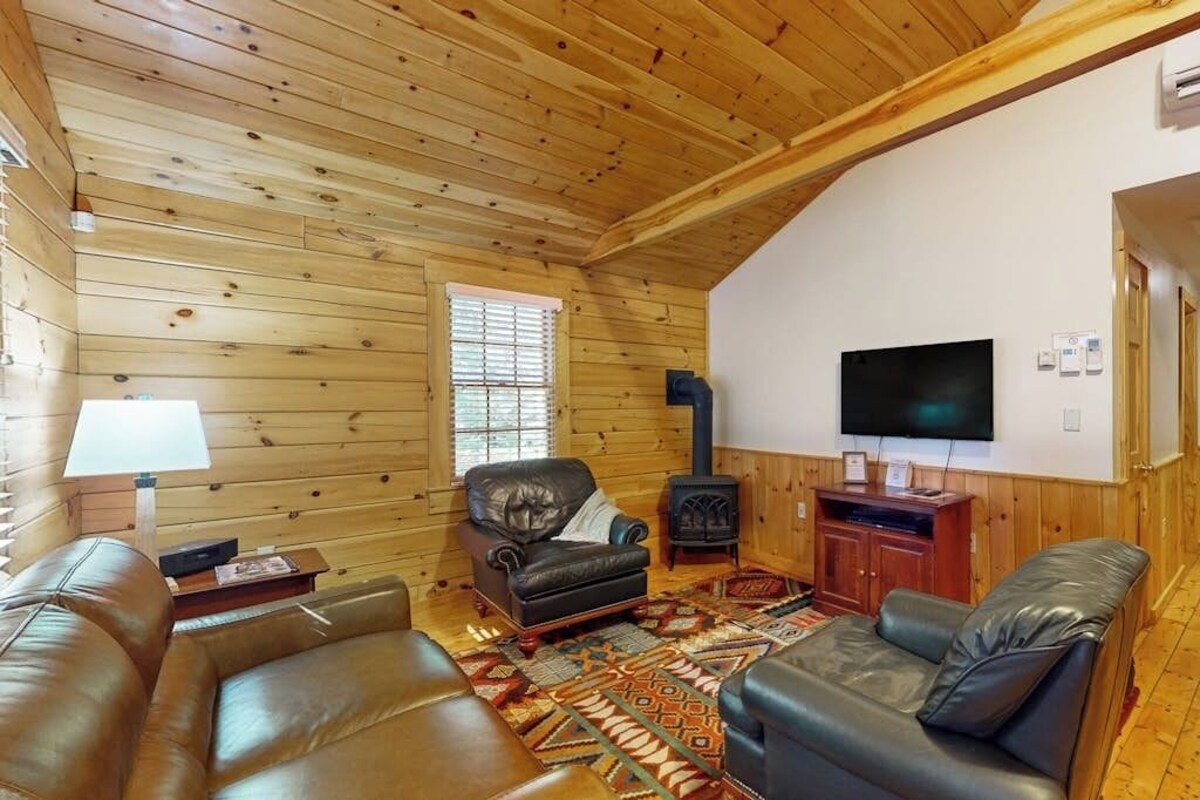 Interior de una cabaña de troncos con chimenea, sofás de cuero, televisor y alfombra estampada.