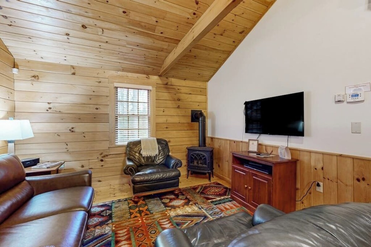 Un interior de cabaña acogedor con techo de madera, chimenea, televisor y mobiliario de cuero.