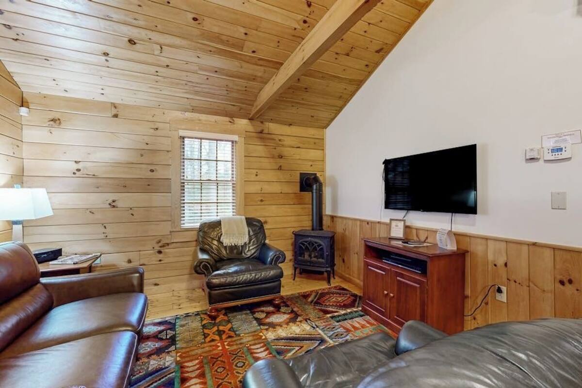 Un interior de cabaña acogedor con techo de madera, chimenea, televisor y mobiliario de cuero.