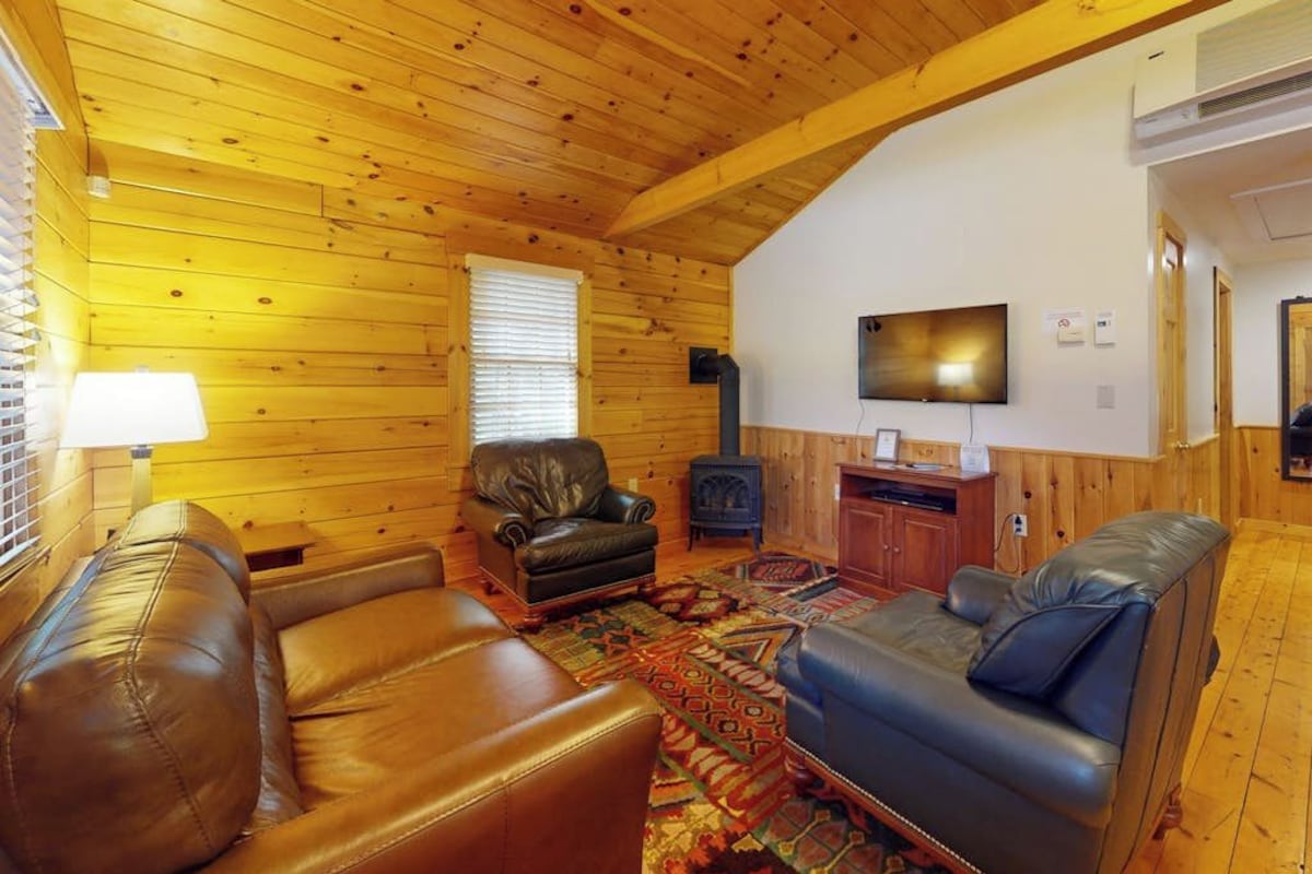 A cozy log cabin interior with a fireplace, leather sofas, and a television.