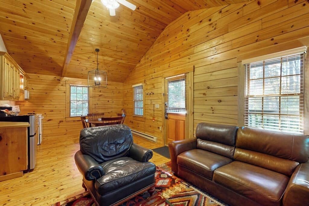 A log cabin interior with a dining area, leather seating, and a kitchen.